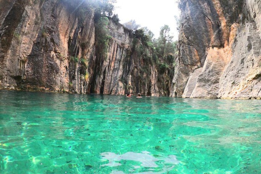 A clear turquoise sea, rocky cliffs, and dense vegetation. 1