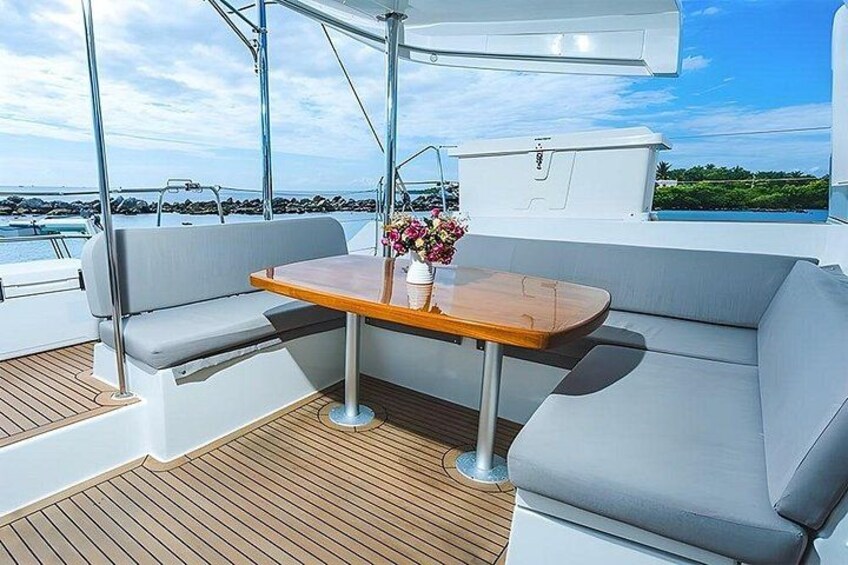 A boat deck with a wooden table, grey cushioned seating, and a flower vase. 3