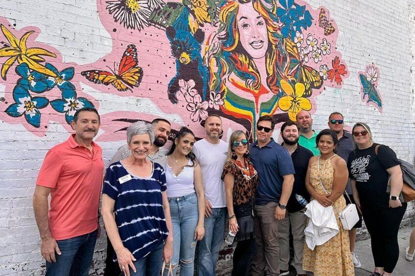 A group of people standing in front of a colorful mural with floral and butterfly designs. 2