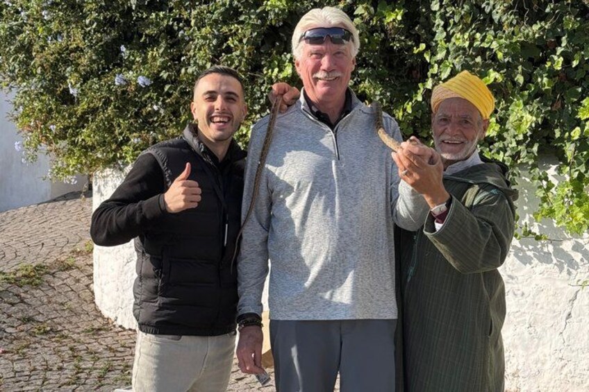 Tres personas de pie al aire libre, con un camino adoquinado y un árbol al fondo. 2