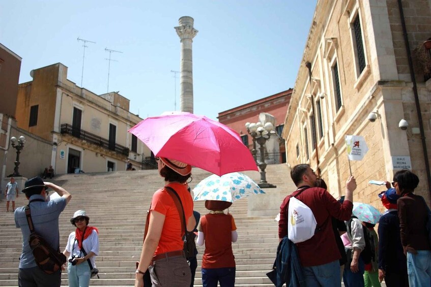 A group of people ascending a set of stairs in an urban area with historical architecture, including a tall column and a building with a sign. 1