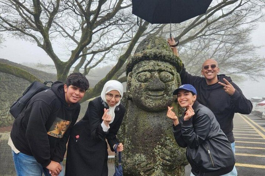 A group of people posing with a moss-covered statue in a parking lot. 5