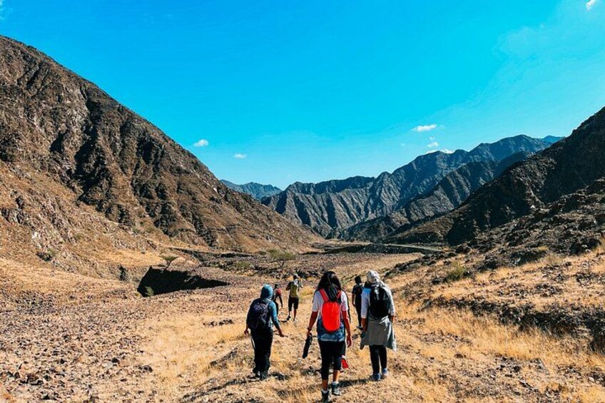 Un groupe de randonneurs marchant sur un sentier rocailleux et aride, avec des montagnes en arrière-plan. 1