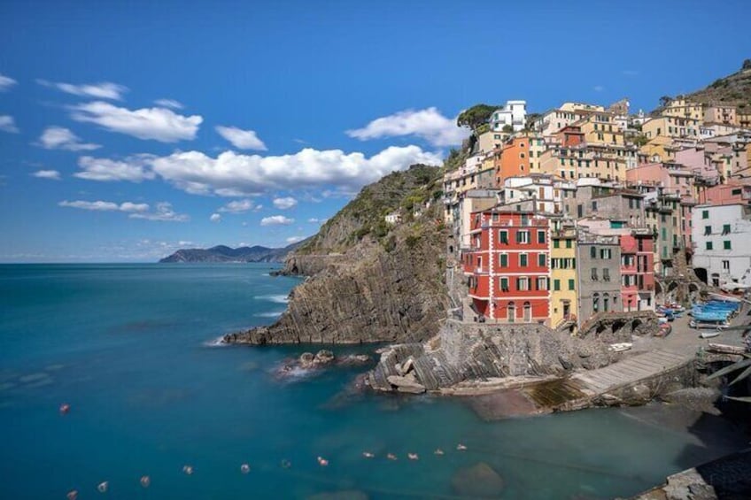 A coastal town with colorful buildings, a rocky shoreline, and clear blue water. 1
