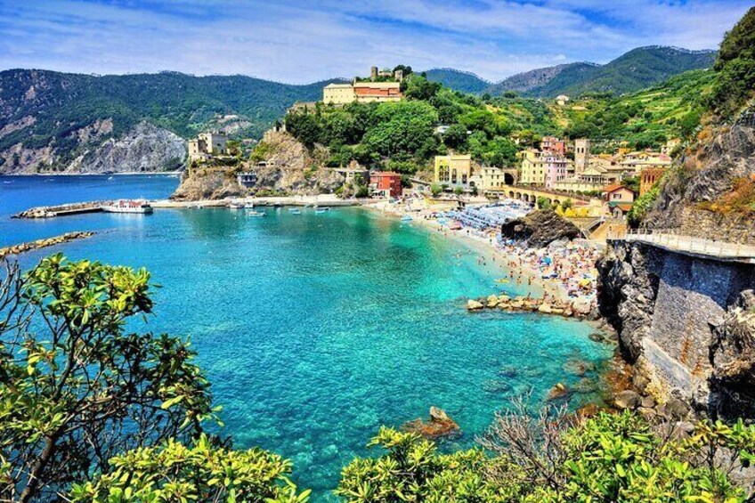 A coastal town with clear turquoise waters, a rocky shoreline, and buildings on a hillside. 2