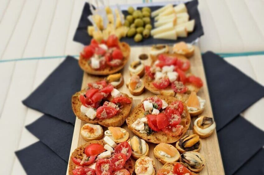 A wooden board with various appetizers including bruschetta topped with tomatoes, cheese, and olives. 4