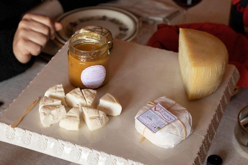 Tagliere con un'ampia fetta di formaggio, un vasetto di miele e diversi bocconcini di formaggio. 3