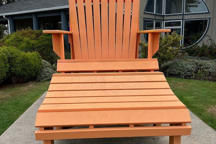 A wooden Adirondack chair with a slatted seat and backrest, positioned on a concrete path. 4