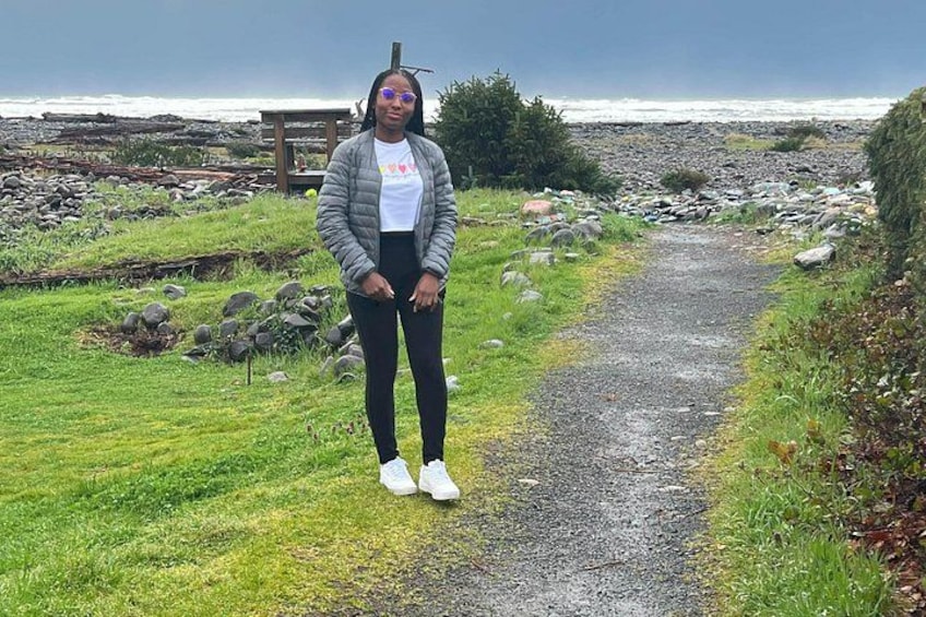 A person standing on a gravel path with grass on either side, a wooden structure in the background, and the ocean in the distance. 5
