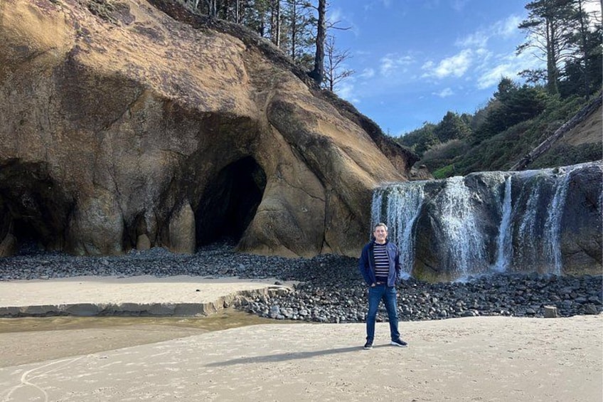 A person standing in front of a large rock formation with a waterfall. 5