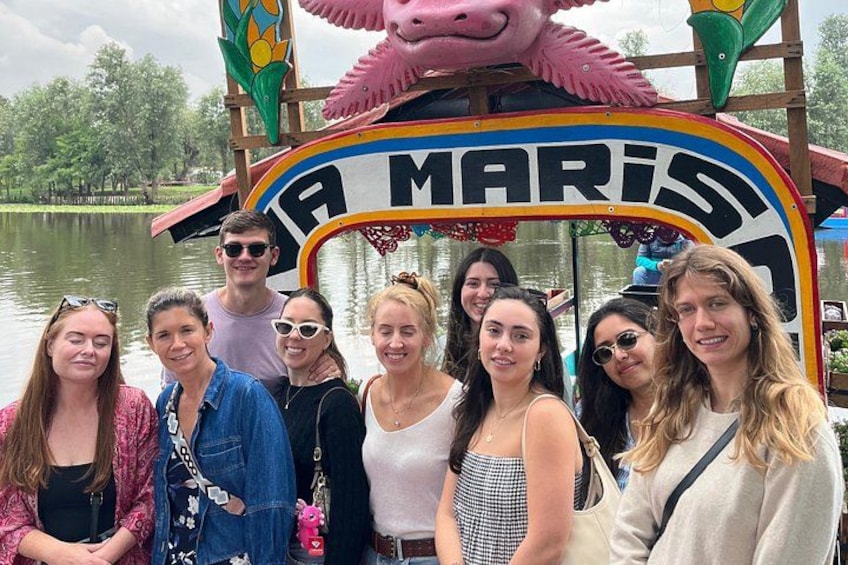 A group of people in front of a colorful boat with the name 'A MARISI' on it, docked by a calm body of water. 4