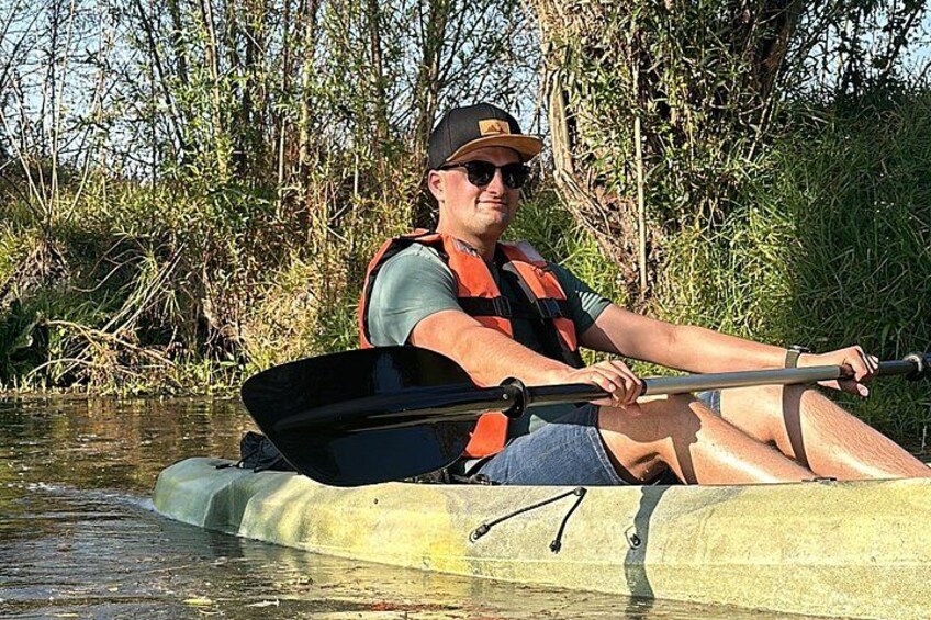 A person in a kayak on a river surrounded by vegetation. 2