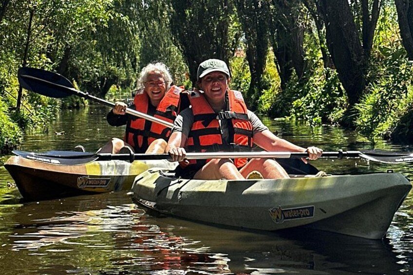 Two people kayaking on a river surrounded by dense greenery. 3