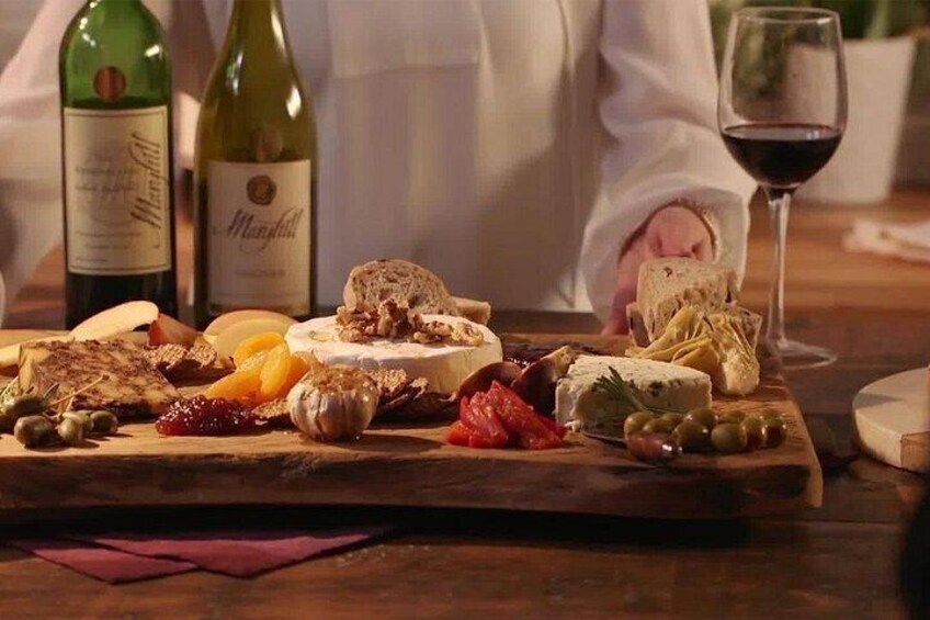 A charcuterie board with various cheeses, meats, and olives, accompanied by wine bottles and a glass of red wine. 4
