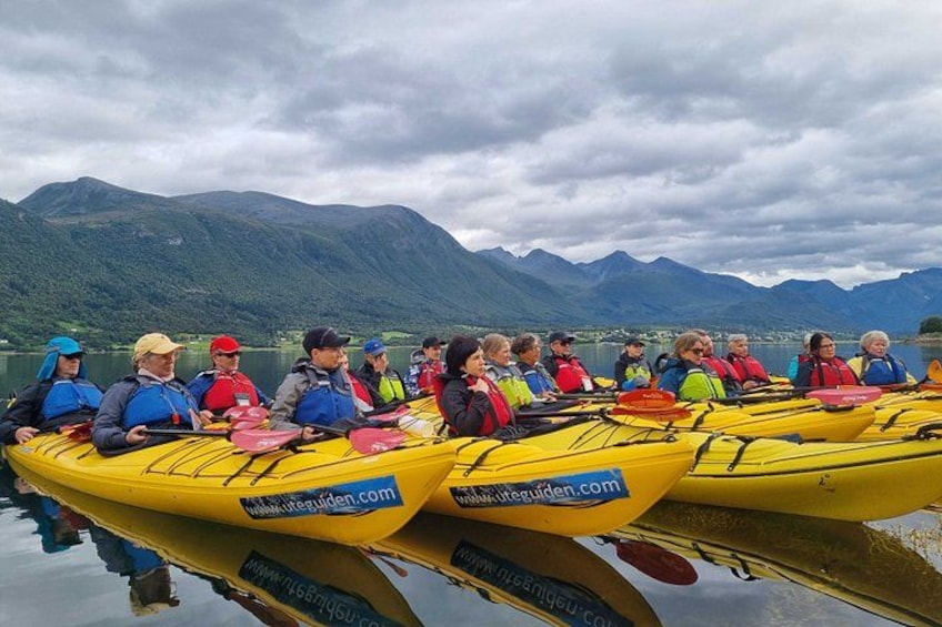 A group of people in yellow kayaks on a calm lake with mountains in the background. 2