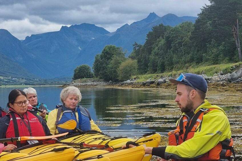 A group of people in a yellow kayak on a calm lake with mountains in the background. 3