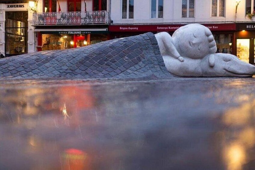 A sculpture of a sleeping figure on a sloped surface with reflections in the water below. 1