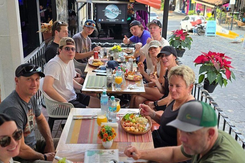 Un groupe de personnes est assis à la terrasse d’un restaurant, avec vue sur la rue en arrière-plan. 3