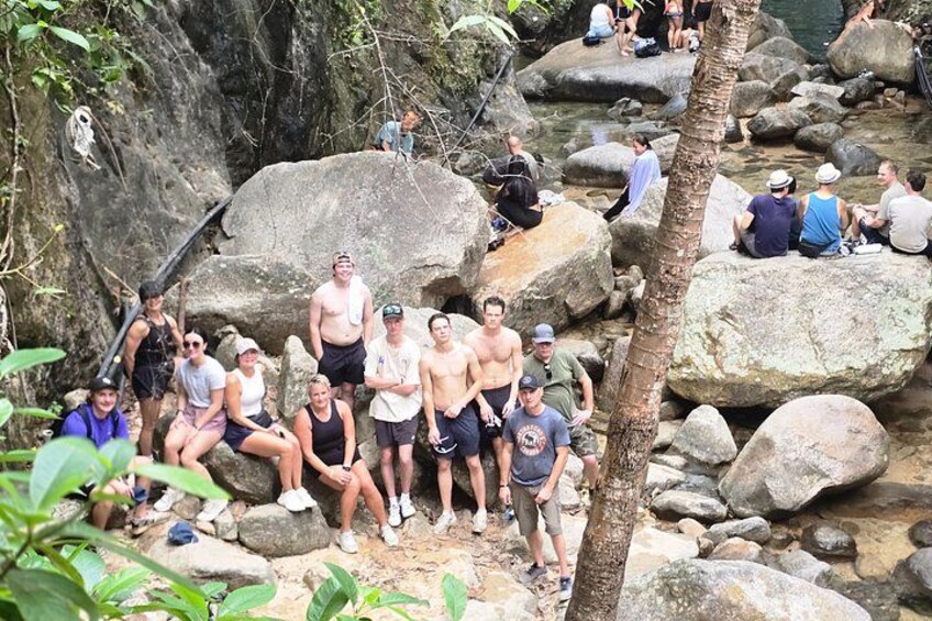 Un groupe de personnes est assis et se tient debout sur des rochers, près d’un ruisseau, dans une zone boisée. 4