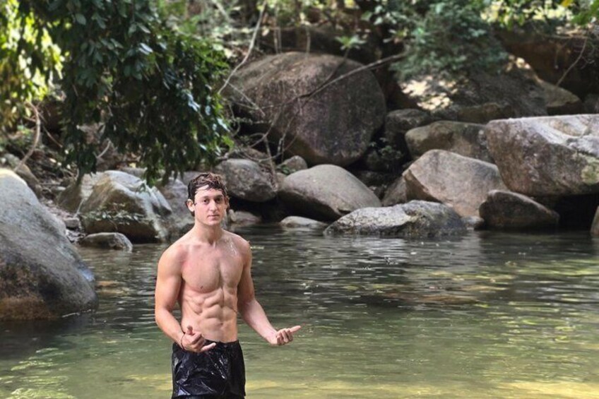 Une personne se tient debout dans un ruisseau aux eaux claires, entourée de gros rochers et de verdure. 4