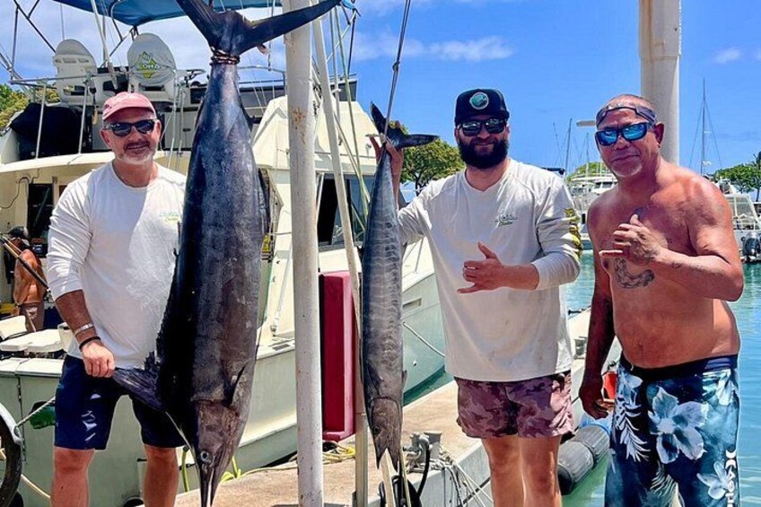 Three people holding large fish on a boat dock. 5