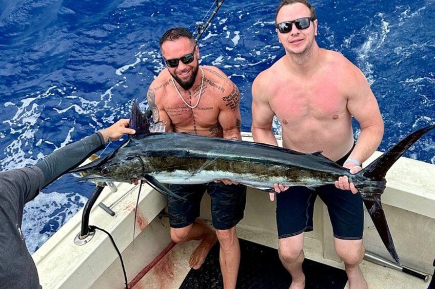 Two men holding a large fish on a boat in the ocean. 4