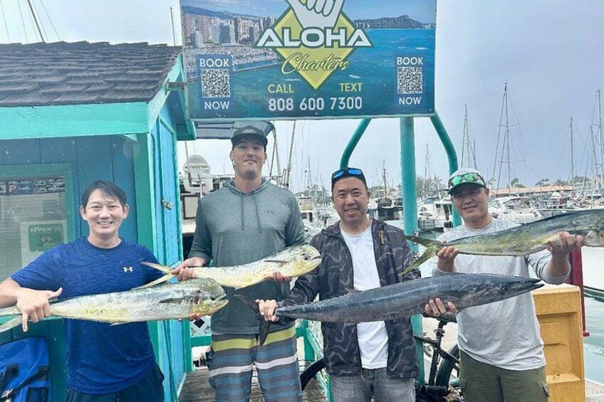 Four people holding large fish in front of a seafood shop. 3
