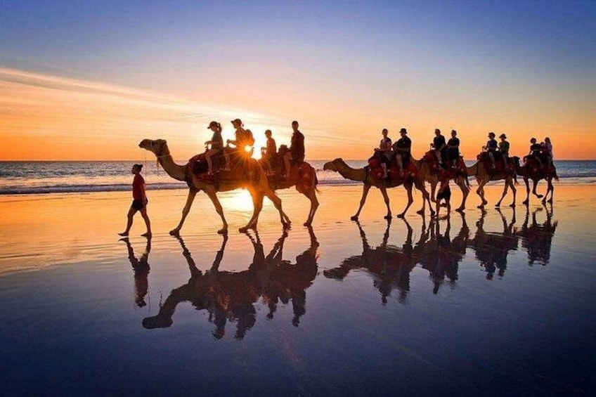 A group of people riding camels on a beach at sunset. 2