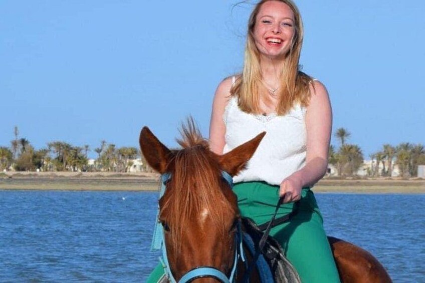 A person riding a horse by a body of water with palm trees in the background. 3