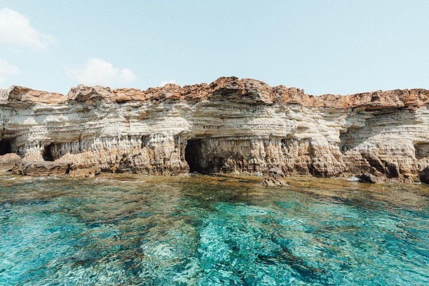 Un acantilado costero con agua azul cristalina y la entrada de una cueva. 2