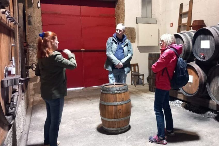Tres personas en una bodega con barriles de madera y una puerta roja. 4