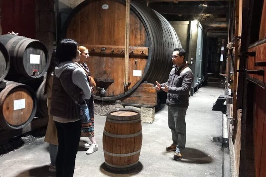 Personas en un sótano con barriles de madera y una gran puerta de madera. 5