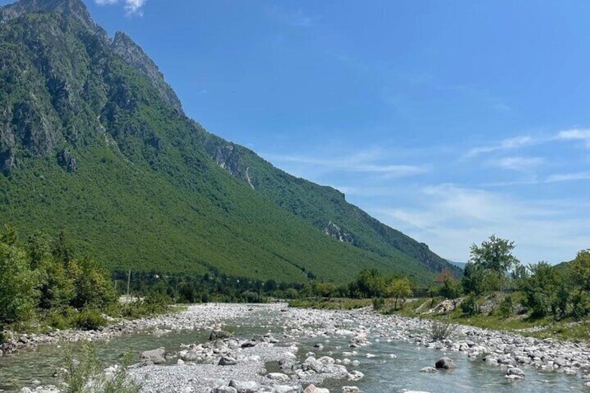 En flod med stenar, omgiven av gröna kullar och ett berg. 5