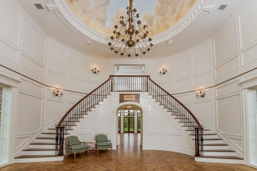 A grand staircase with a chandelier, white paneled walls, and a wooden floor. 4
