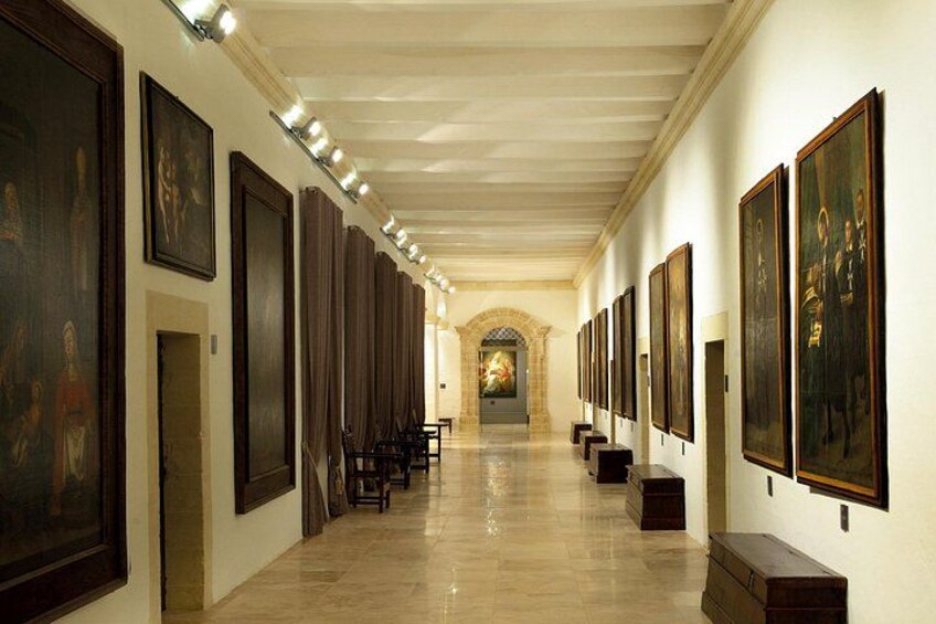 A long hallway with framed artworks on both sides, leading to a central archway. 2