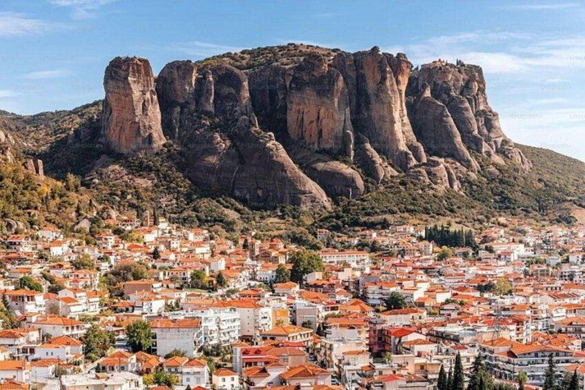 A town with red-roofed buildings and a prominent rocky mountain in the background. 2