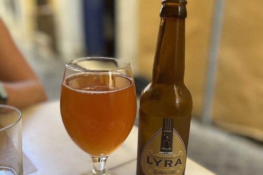 Een glas amberkleurige vloeistof naast een fles met de naam 'LYRA' en een logo. 4