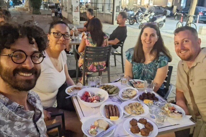 A group of people dining at an outdoor restaurant with various dishes on the table. 1
