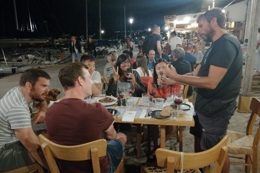 A group of people dining outdoors at night with a waterfront view. 3