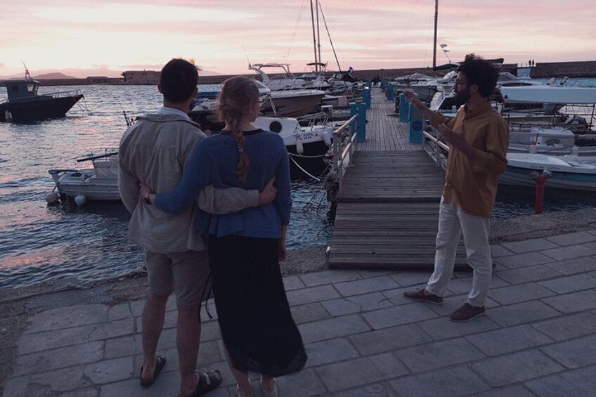 A pier with boats, a sunset, and people standing by the water. 2
