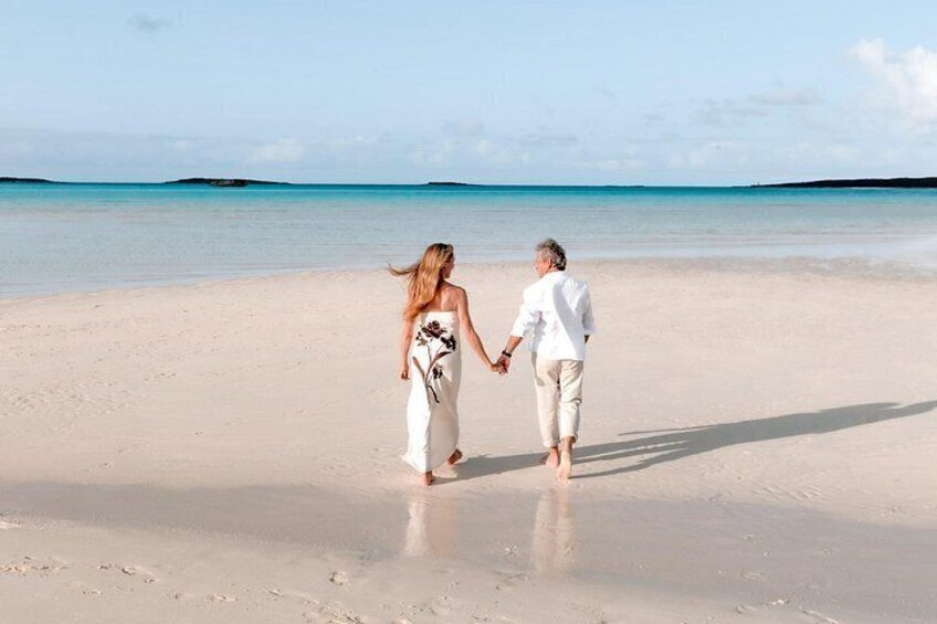 A couple walking on a sandy beach with a calm sea and clear sky in the background. 2