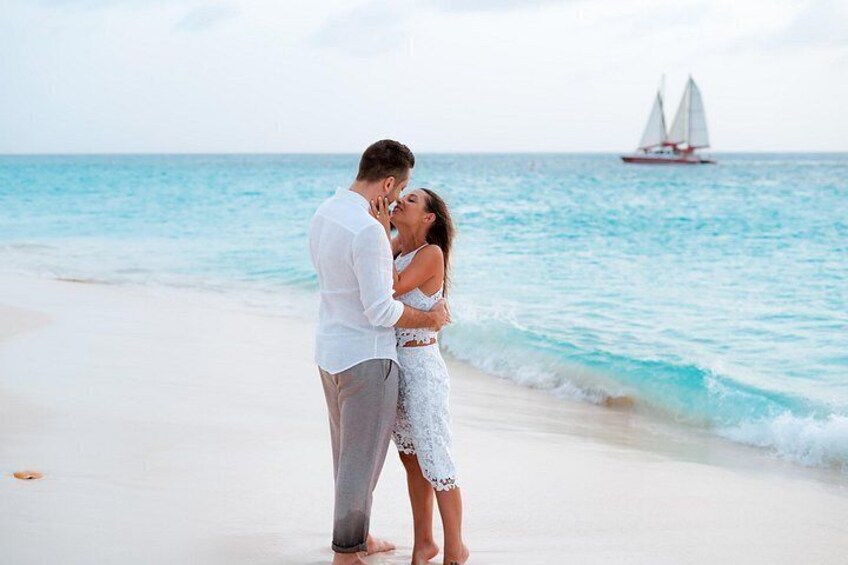 A couple embracing on a beach with a sailboat in the background. 1
