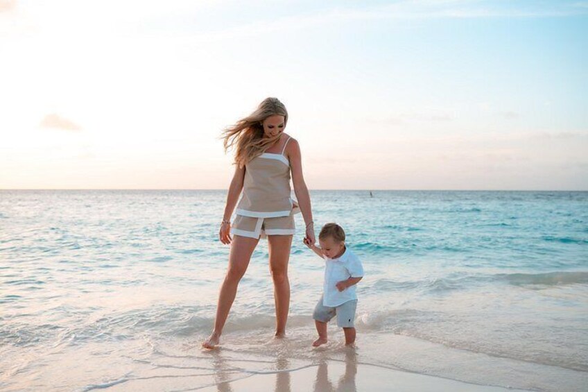 A woman and a child walking on a beach with the ocean in the background. 4