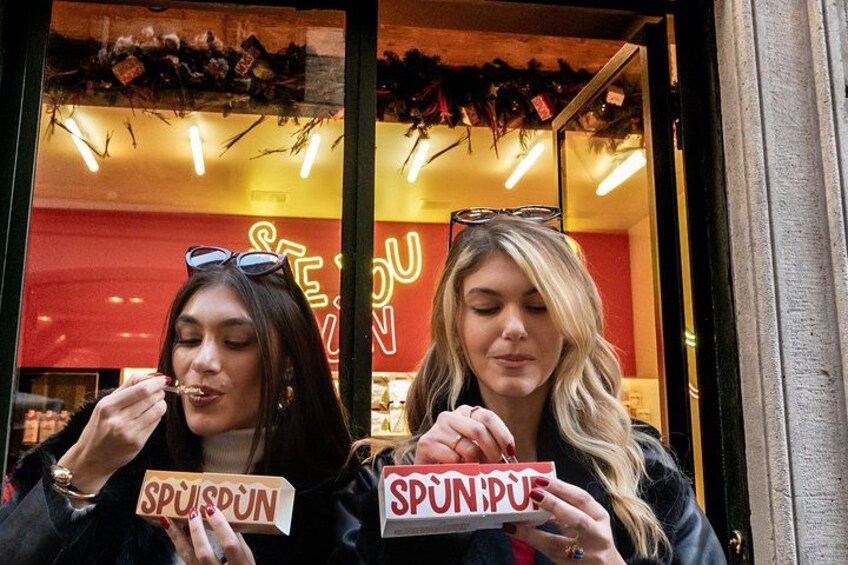 Two individuals holding signs in front of a store with a red interior. 2