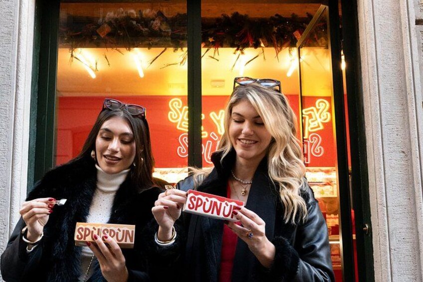 Two people holding signs in front of a brightly lit storefront with a red and yellow sign. 1