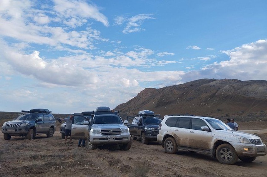 A group of vehicles parked on a dirt road in a desert landscape with mountains in the background. 2