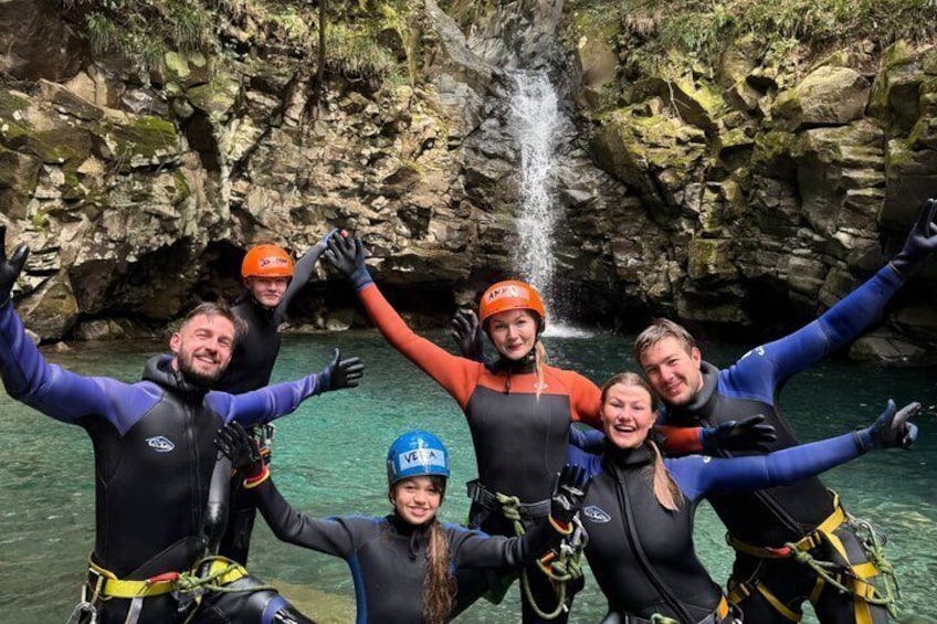 A group of people in wetsuits and helmets near a waterfall in a rocky area. 3