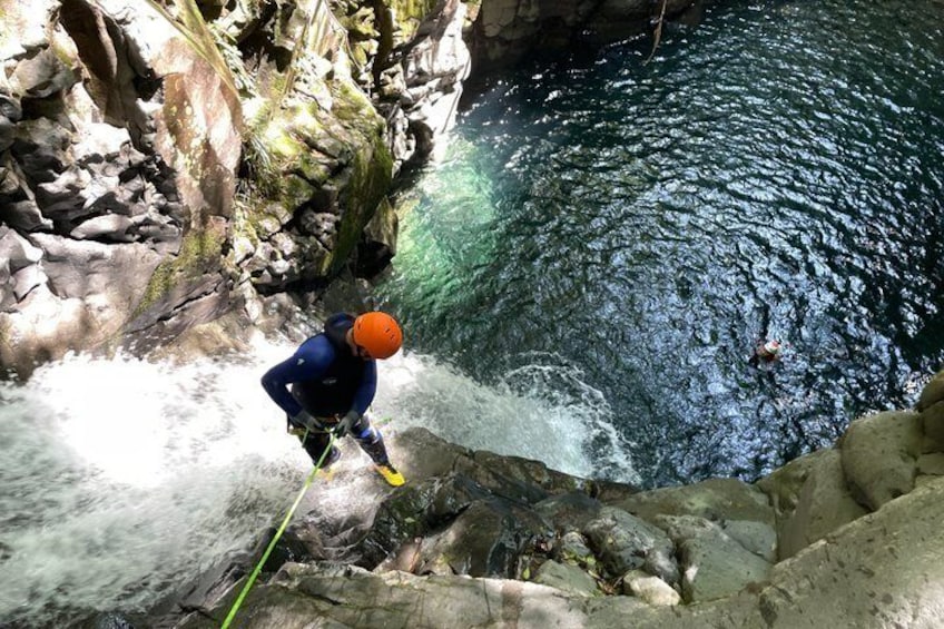 A person rappelling down a rocky cliff into a body of water. 2