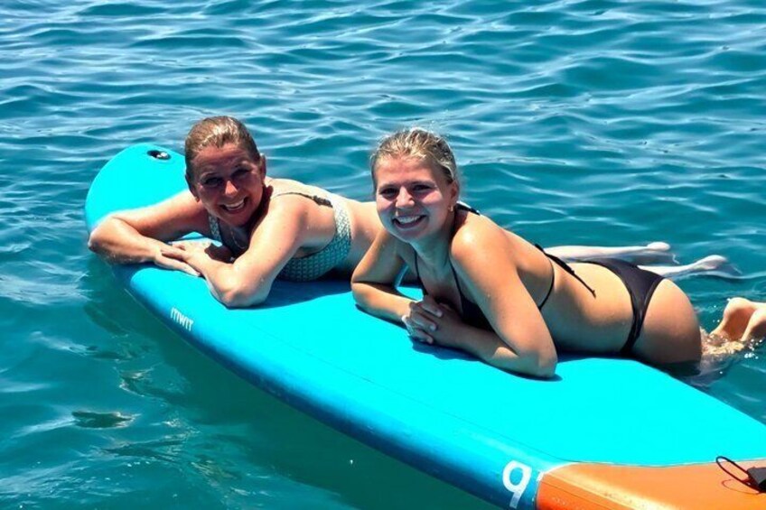 Two people lying on a blue floating board in the water. 3
