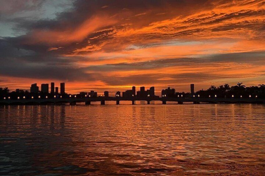 A sunset over a city skyline with a bridge and water reflecting the sky. 2